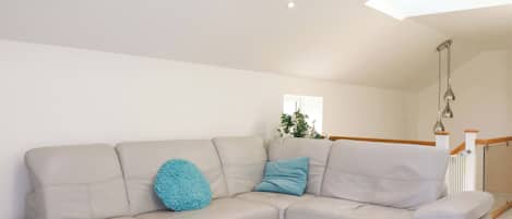 A modern living room with a light-colored sectional sofa, a small round blue accent pillow, and a wooden staircase in the background.