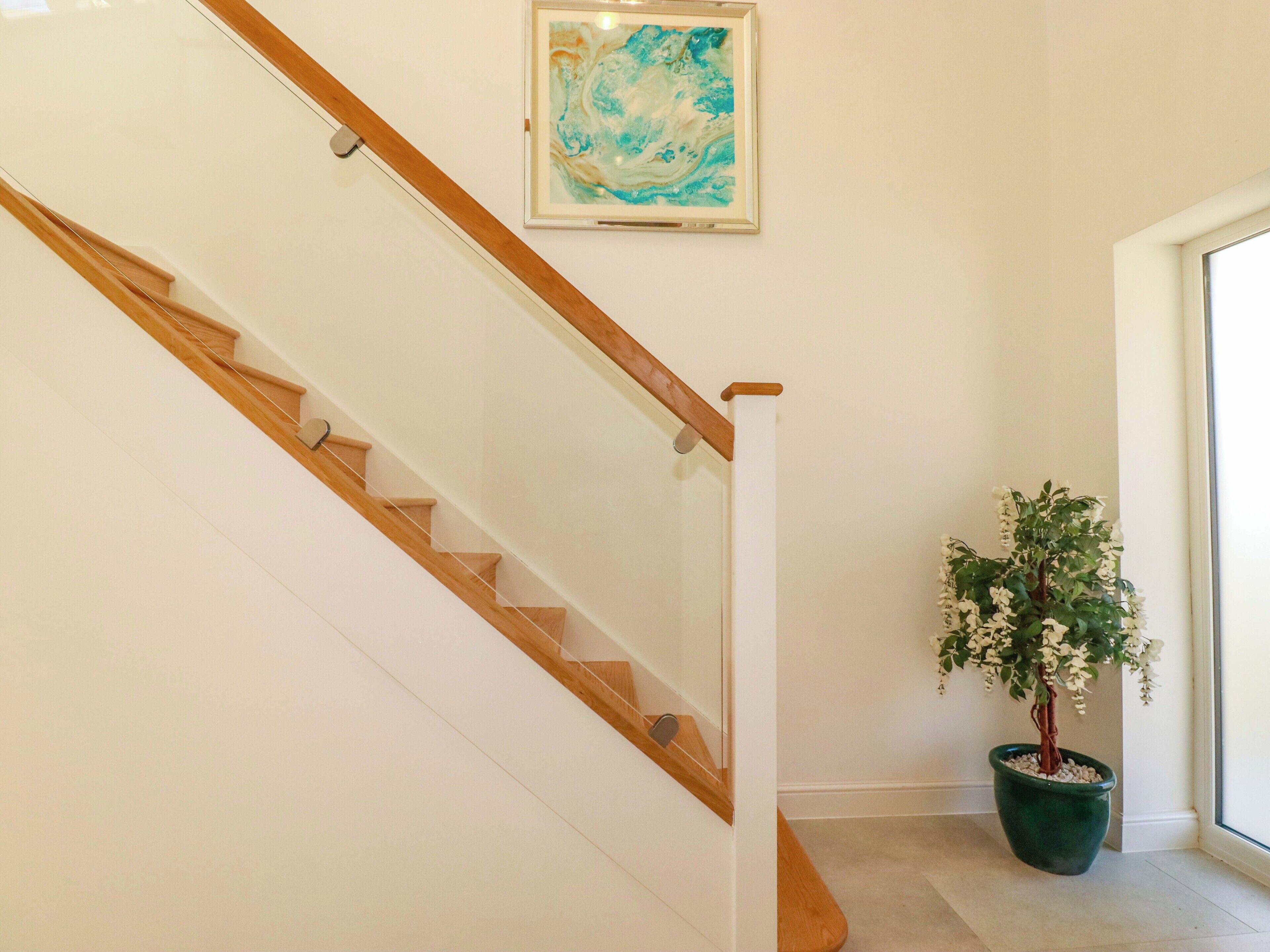 A staircase with wooden steps and a glass railing, a framed abstract painting on the wall, and a potted plant with white flowers.