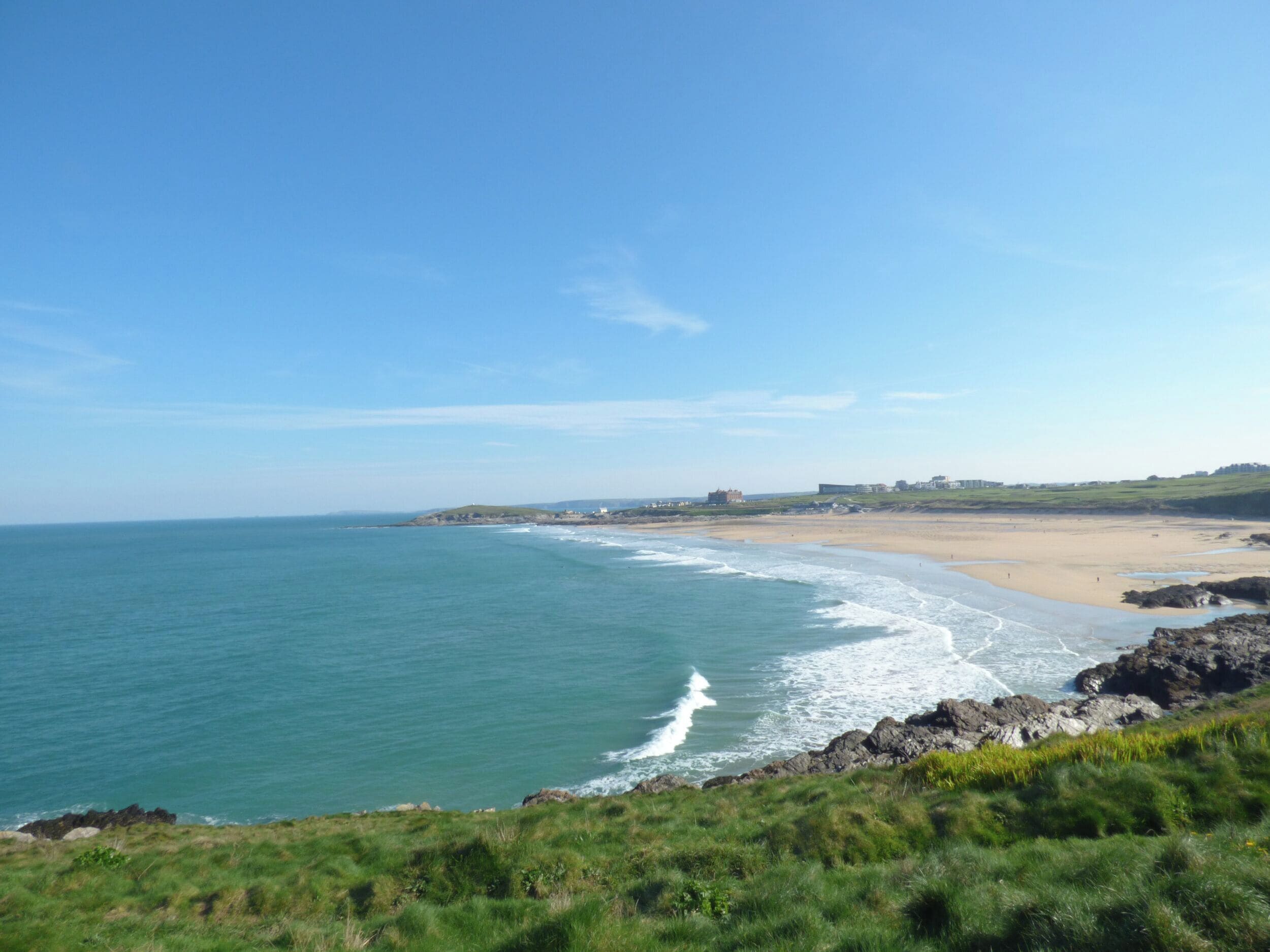 Paisaje costero con playa, costa rocosa y edificios al fondo.