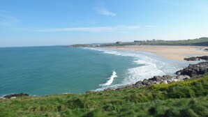 Paisaje costero con playa, costa rocosa y edificios al fondo.