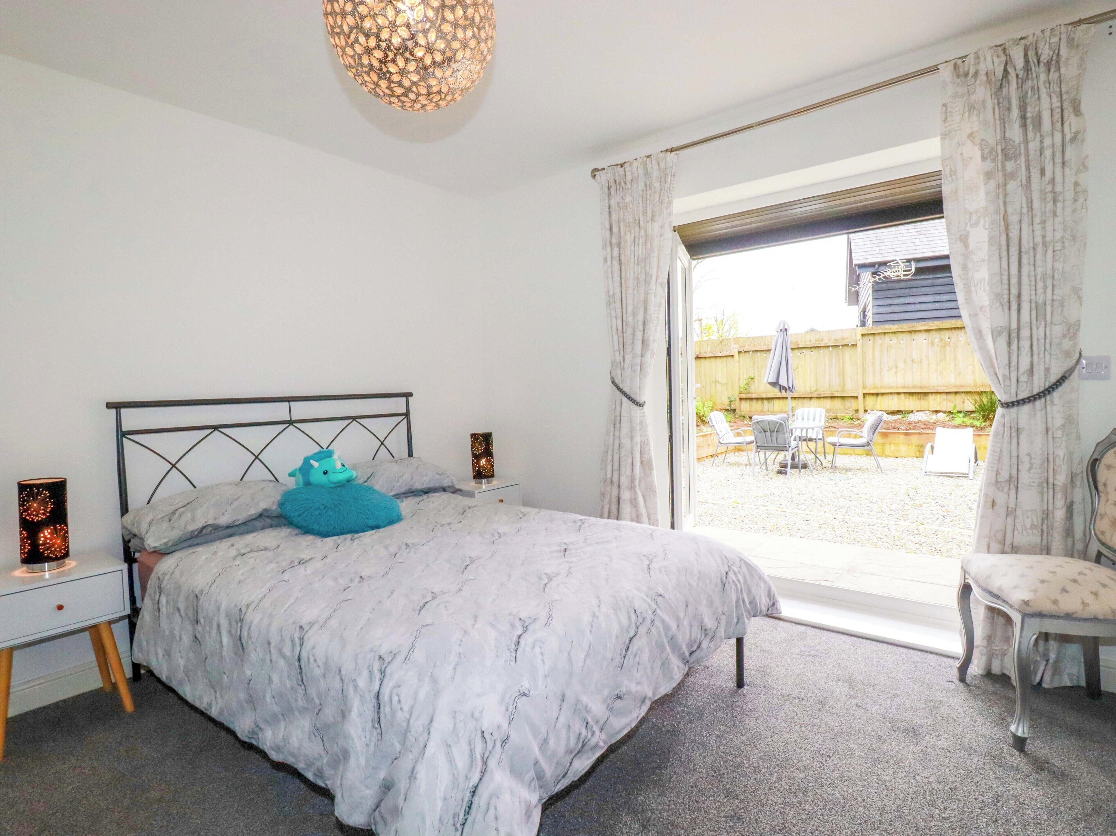 Une chambre à coucher comprenant un lit, des tables de chevet, une commode, une fenêtre avec des rideaux et une vue sur le jardin arrière.