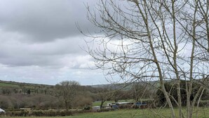 Un paisaje rural con un área cercada, un árbol y edificios a la distancia.