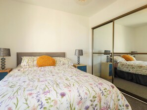 A bedroom with a large bed, two bedside tables, a mirror, and a wardrobe. - Meadow Retreat (Bodmin)