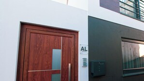 A wooden door with a glass panel, a sign with 'AL' and 'Apartamentos Locales', and a small electronic device on the wall. - Travessa Apartments 1 Bedroom By PontaNegraAzores (Praia da Vitória)