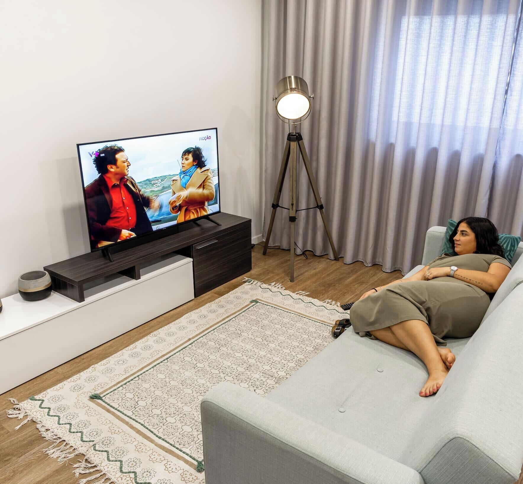 Un salón con un televisor de pantalla plana, una lámpara con trípode y un sofá.
