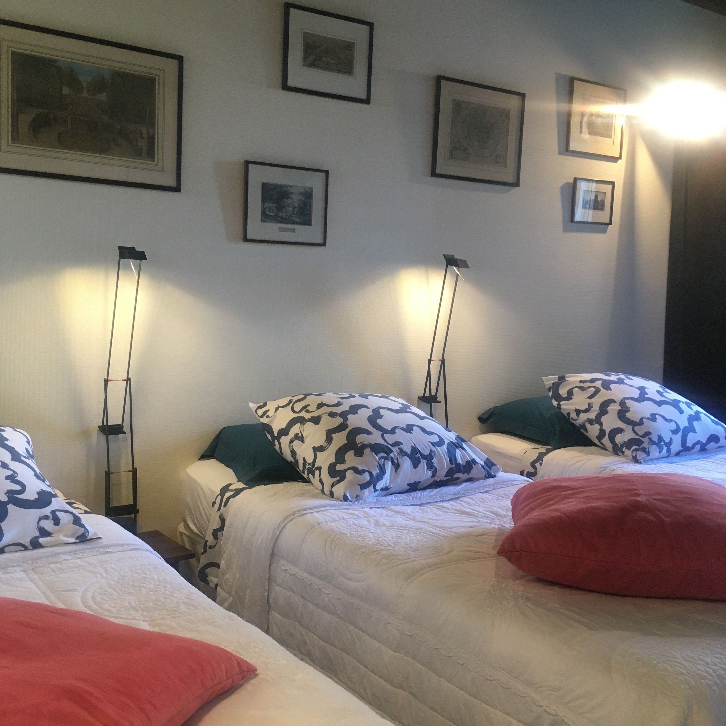 Une chambre d’hôtel avec trois lits, chacun agrémenté de draps et d’oreillers à motifs, d’un lampadaire et de tableaux encadrés accrochés au mur.