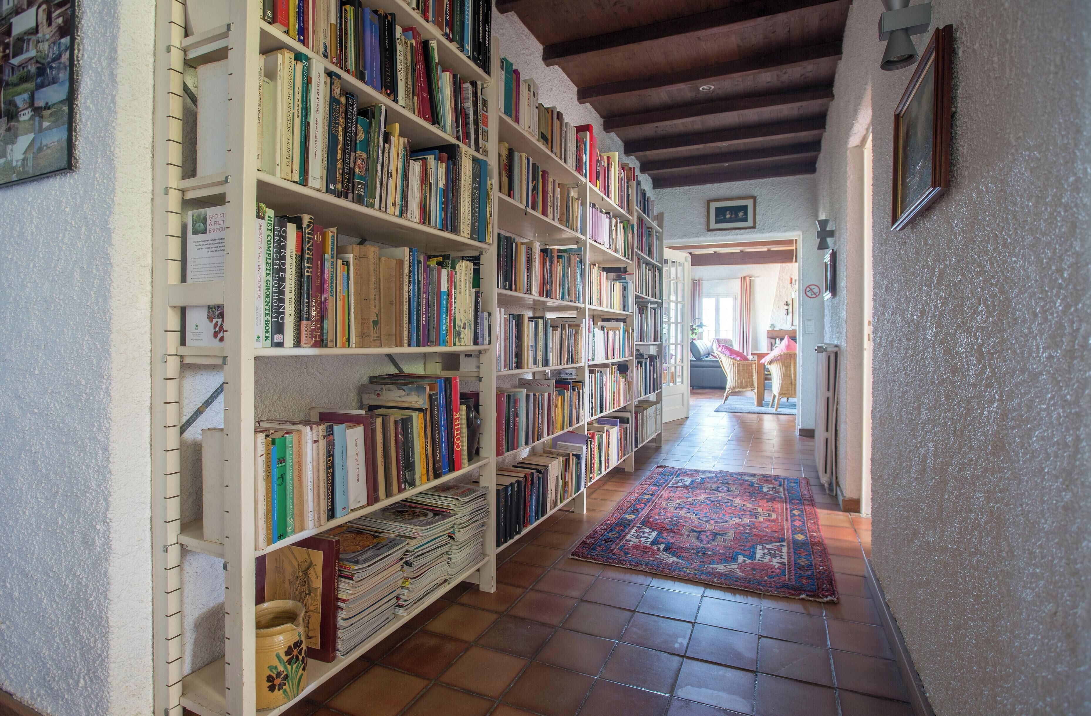 A library with bookshelves filled with books, a patterned rug on the floor, and a wooden ceiling.