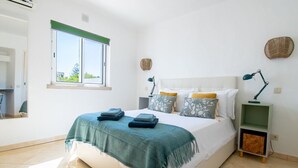 Un dormitorio con cama, mesita de noche, lámpara, ventana y una cesta fijada a la pared.