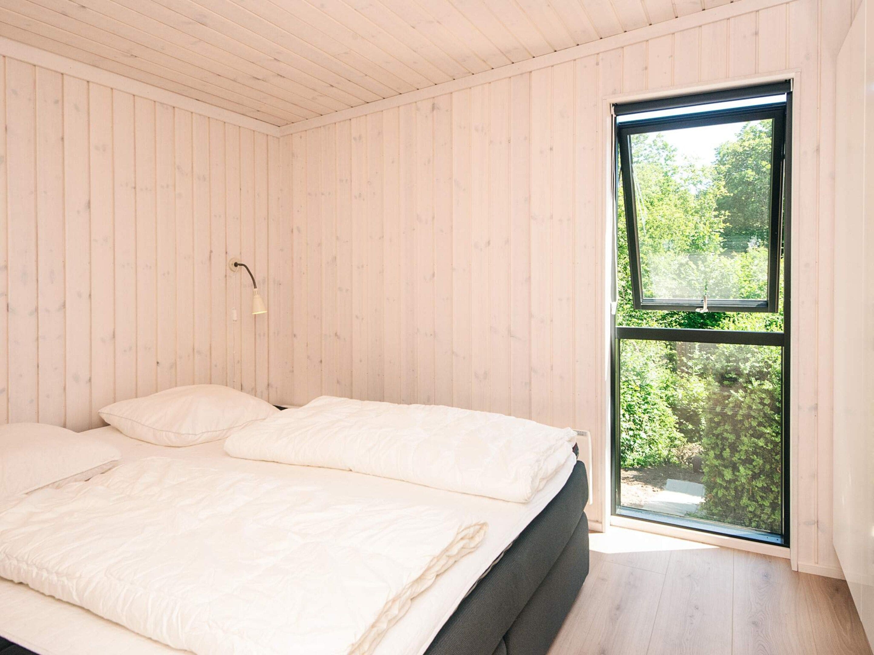 A bedroom with a bed, a window, and wooden walls.