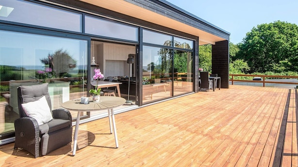 Eine moderne Außenterrasse mit Holzfußboden, einem gläsernen Wintergartenbereich und einer Sitzecke mit Tisch und Stühlen.