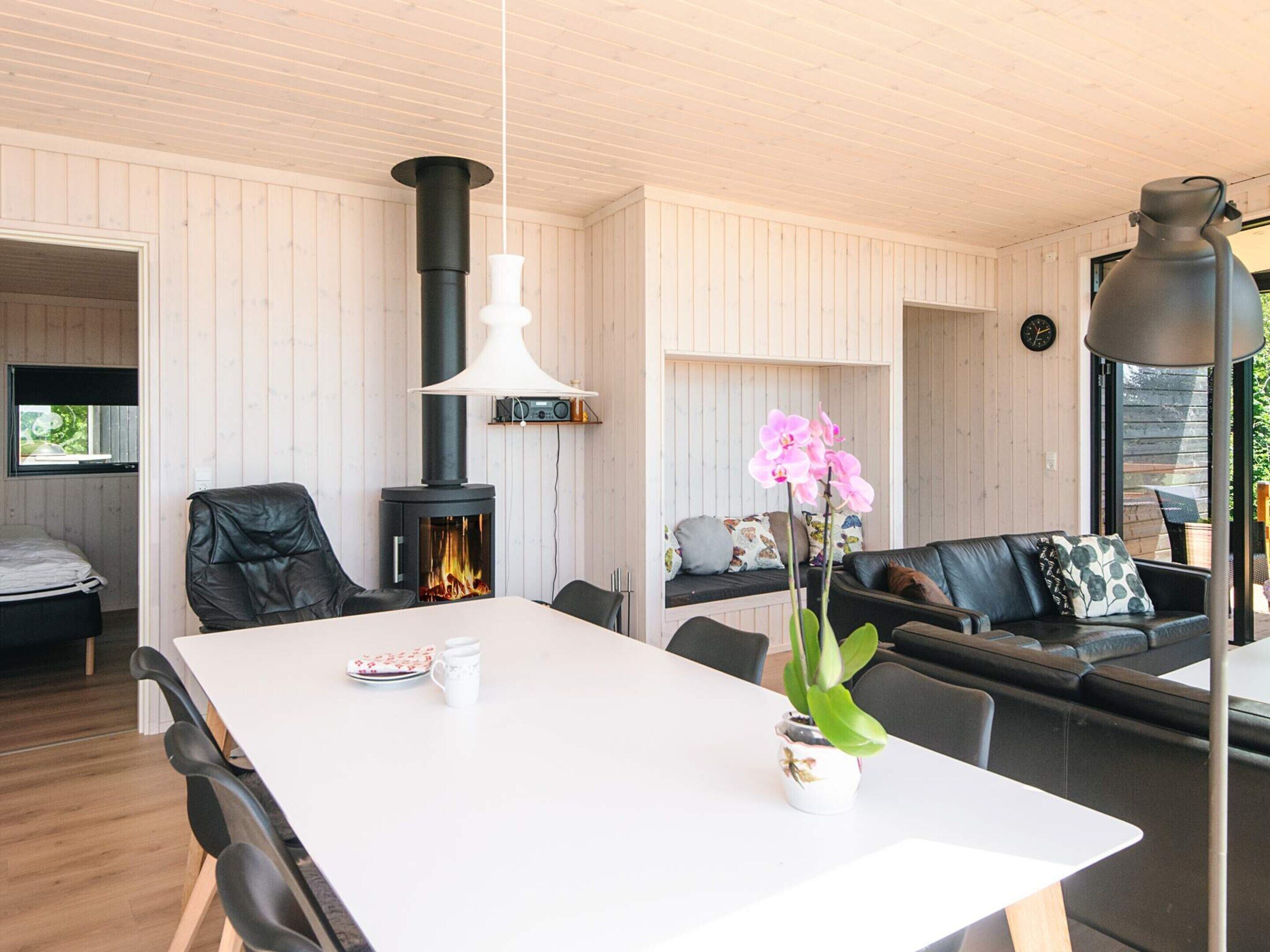Ein modernes Interieur mit einem weißen Tisch, schwarzen Ledersesseln, einer Couch, einer weißen Vase mit Blumen, einem schwarzen Heizkörper und einer Uhr an der Wand.