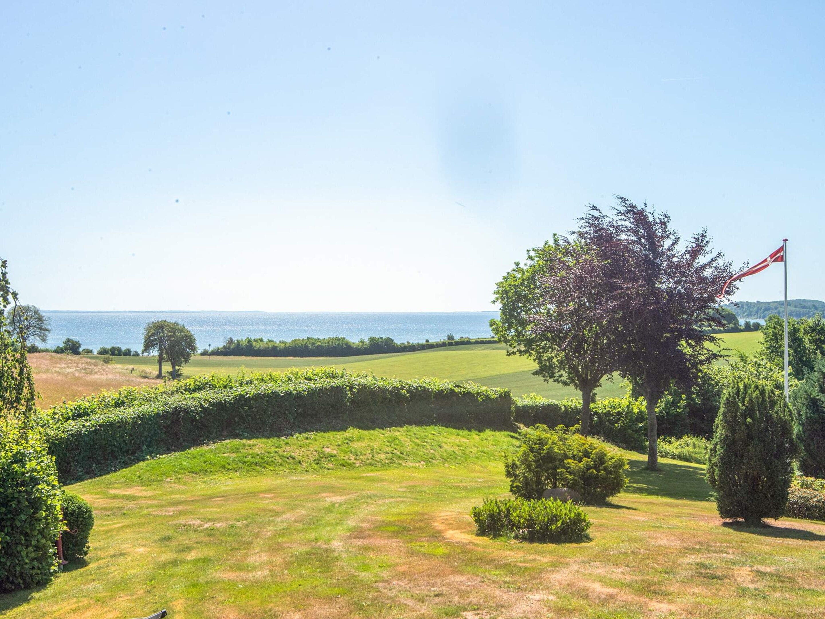 A golf course with a flag, trees, and a view of the sea.