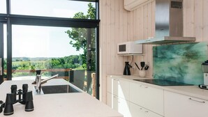 Eine moderne Küche mit einem großen Fenster, weißen Schränken und Blick ins Grüne.