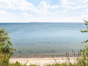 Une plage à l’eau claire, avec un rivage sablonneux et une île qui se dessine à l’horizon.