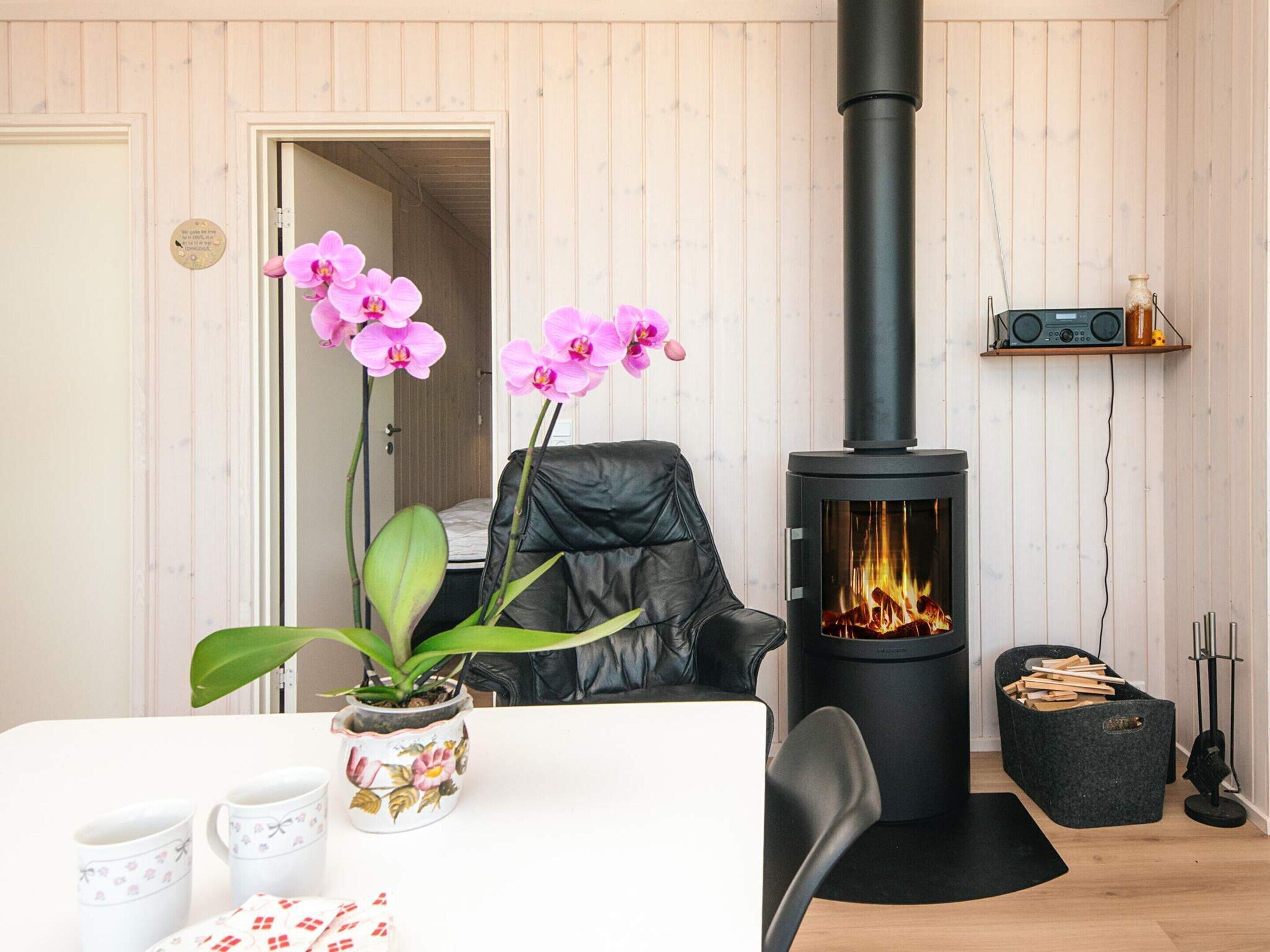 Een kamer met een zwarte leren stoel, een tafel met een bloevas, een zwarte verwarming en een plank met een radio.