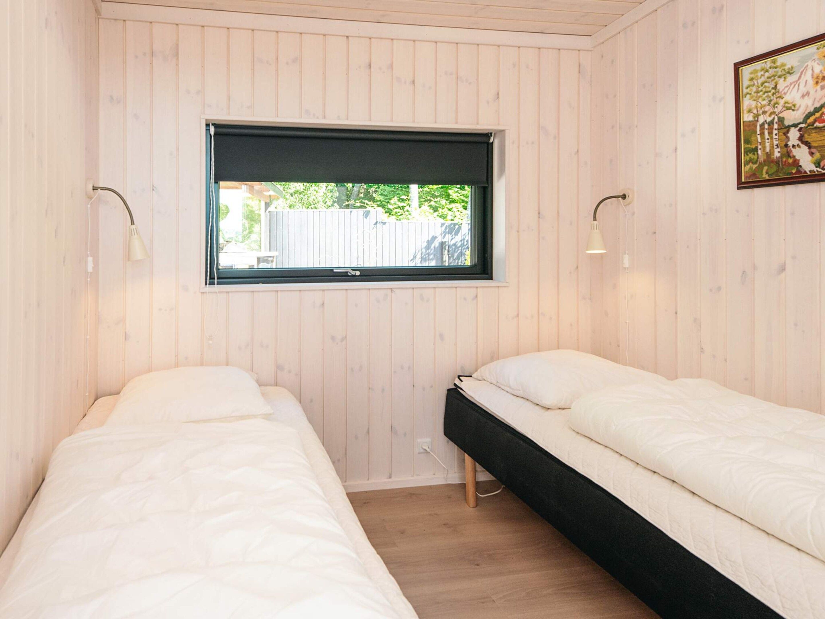 Une chambre avec deux lits simples, une fenêtre avec un store noir et un tableau au mur.