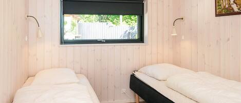 Une chambre avec deux lits simples, une fenêtre avec un store noir et un tableau au mur.
