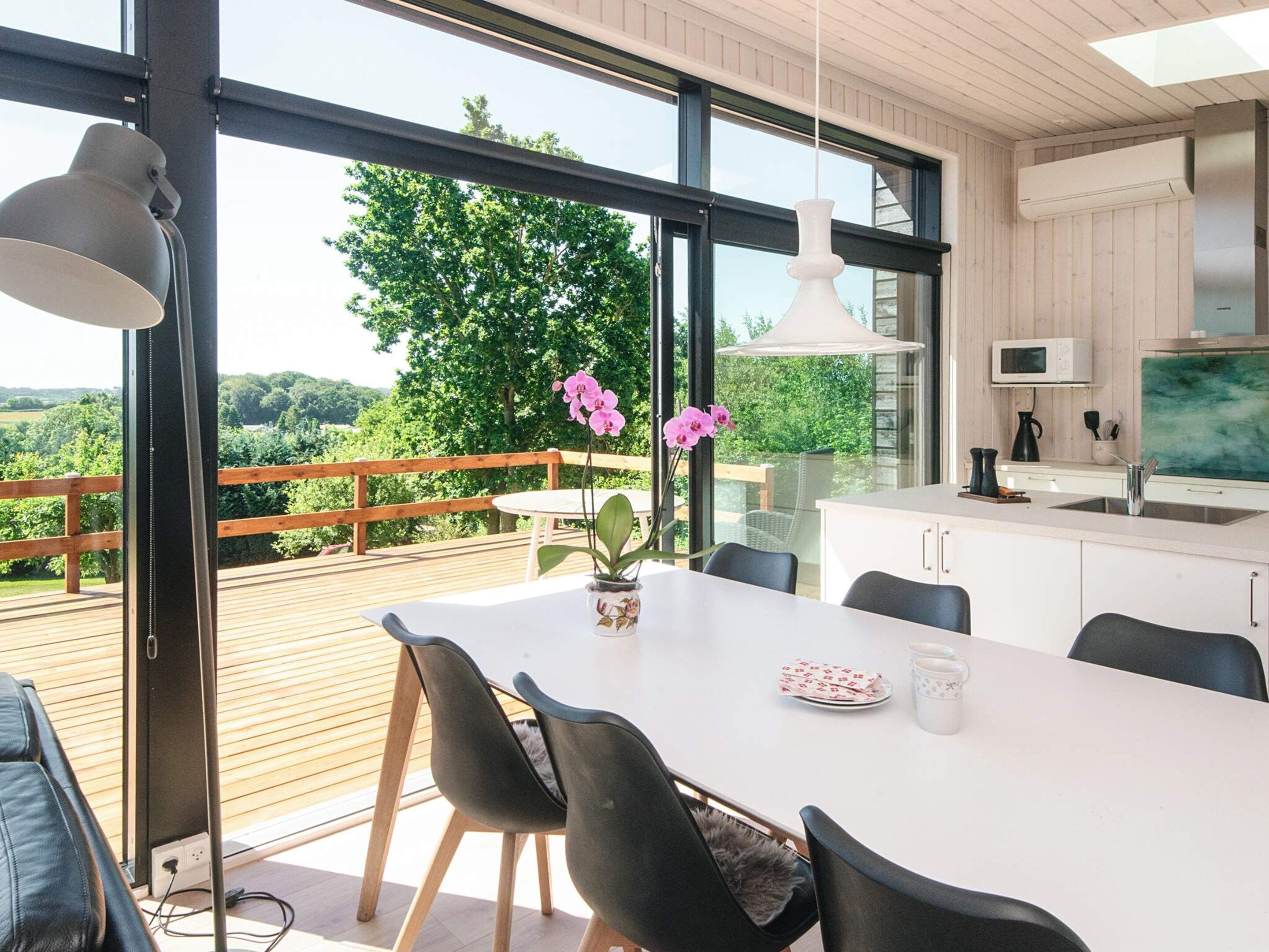 A modern kitchen with a large window, a dining area with a table and chairs, and a wooden deck.