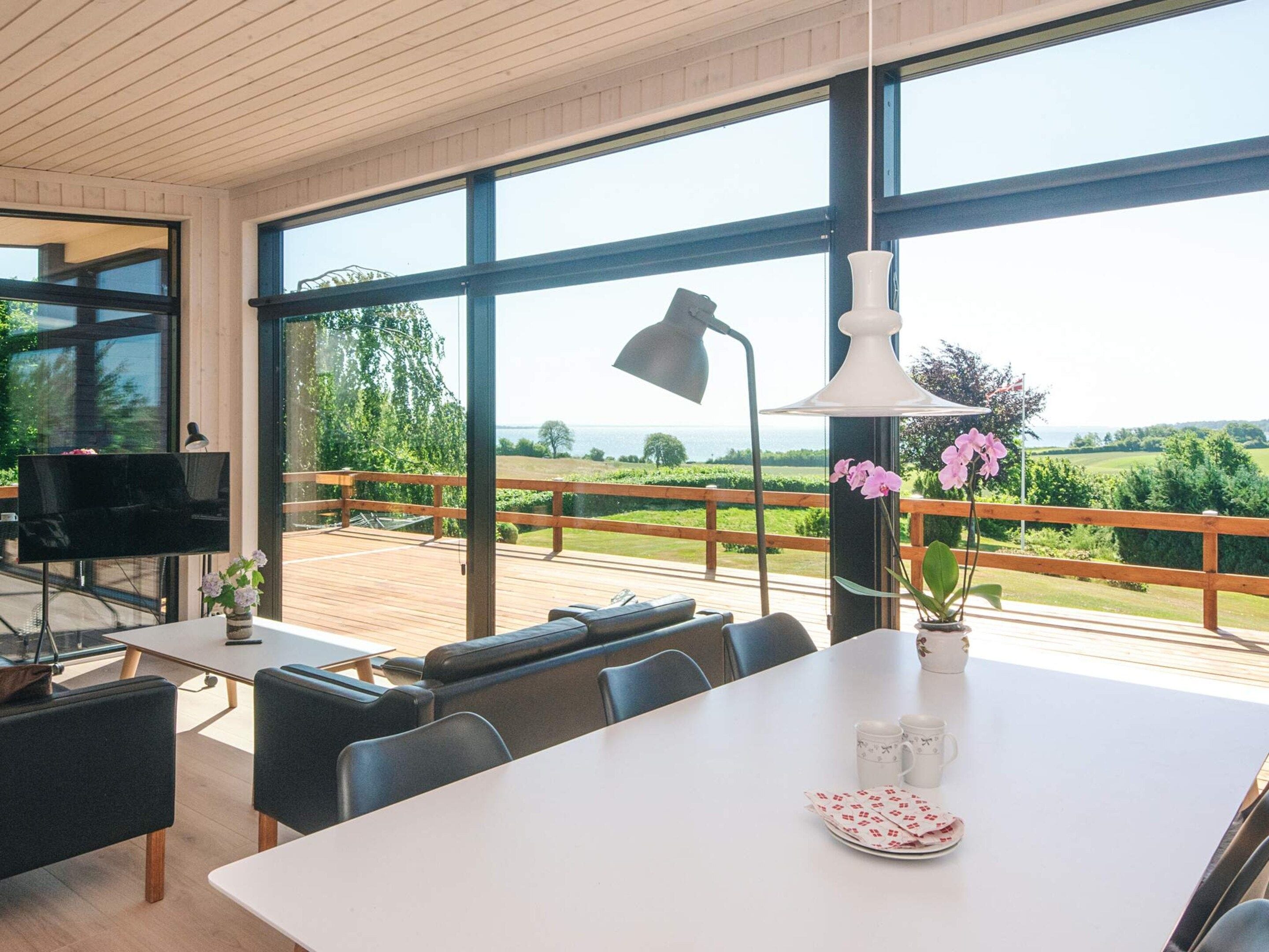 A modern dining area with a large table, chairs, a television, and a view of the outdoors.