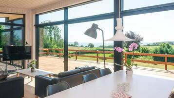 A modern dining area with a large table, chairs, a television, and a view of the outdoors.