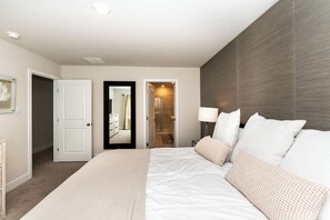 A bedroom with a large bed, a bedside table, a mirror, and a door leading to a bathroom.