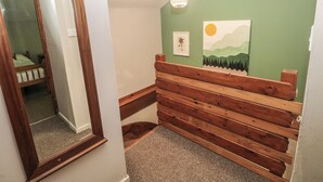 A hallway with a wooden bench, a mirror, a painting of a landscape, and a hanging light fixture. - Cabin No. 2 - Salt and Fern Cabins (Port Talbot)