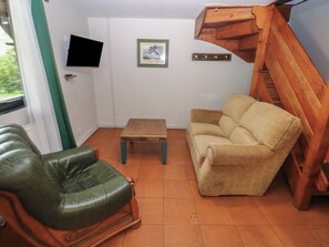 Un salon avec un fauteuil en cuir vert, un canapé beige, une table basse en bois, un téléviseur fixé au mur et un tableau encadré.