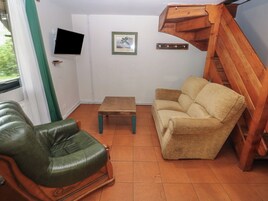 Una sala de estar con un sillón de cuero verde, un sofá color beige, una mesa de centro de madera, un televisor montado en la pared y un cuadro enmarcado.