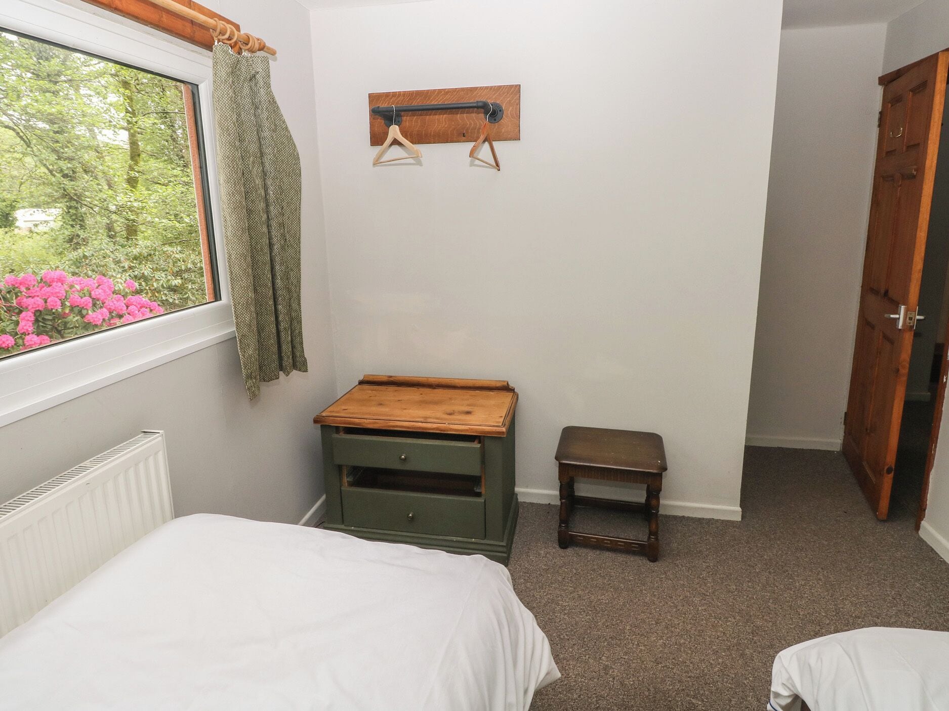 A bedroom with two beds, a small wooden table, a radiator, and a window with curtains.