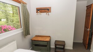 A bedroom with two beds, a small wooden table, a radiator, and a window with curtains. - Cabin No. 2 - Salt and Fern Cabins (Port Talbot)