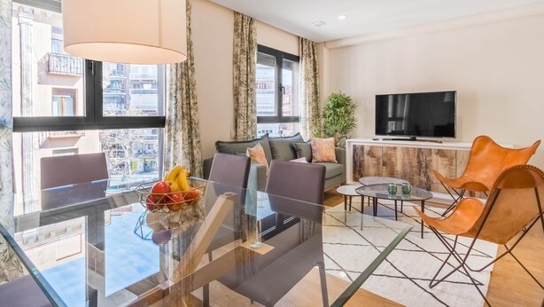 Una sala de estar moderna con una mesa de comedor de vidrio, sofás, un televisor y vistas a la ciudad.