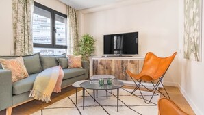 Una sala de estar con un sofá, una mesa de centro, un televisor y una silla.