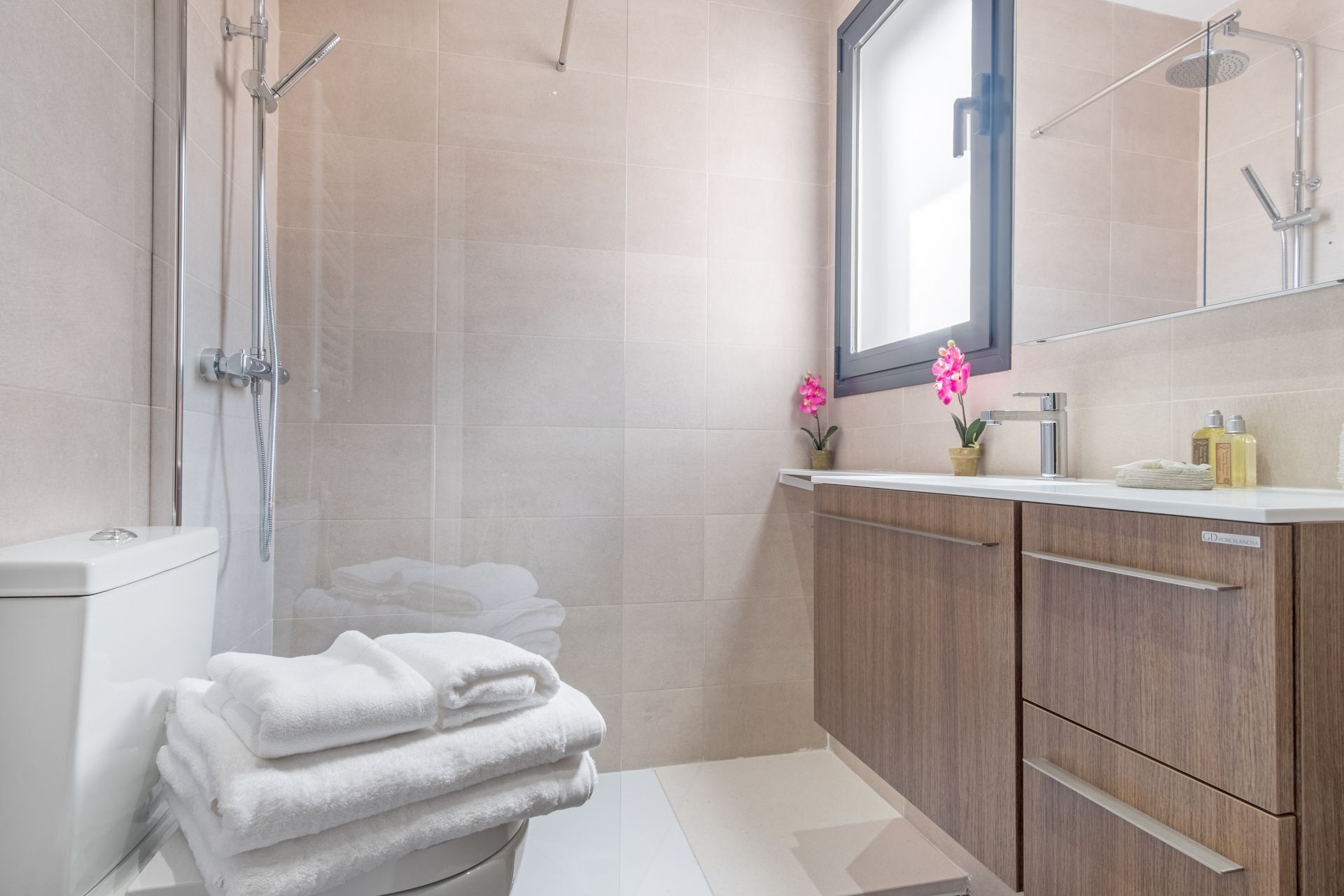 A modern bathroom with a glass shower enclosure, a toilet, a sink with a mirror, and a stack of white towels.