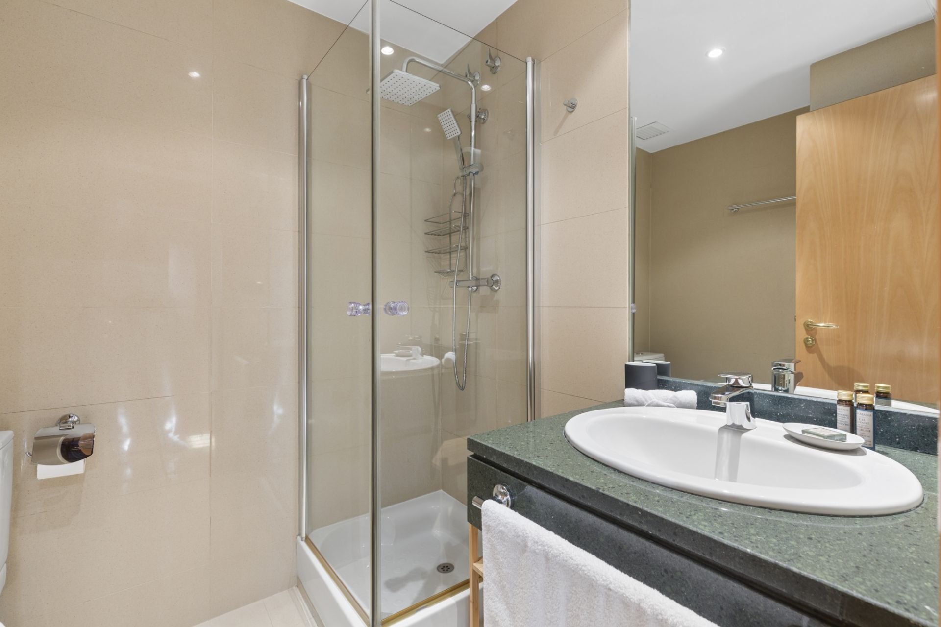 A modern bathroom with a glass-enclosed shower, a sink with a vanity, and a wooden door in the background.