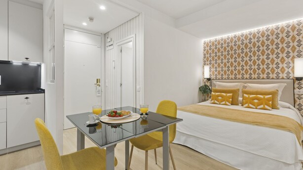 A hotel room with a bed, a dining table with chairs, a TV, and a small kitchen area. - Cozy Studio by Colón & Salamanca District (Madrid)