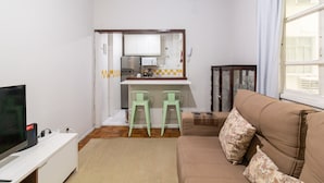 A living room with a television, a sofa, a coffee table, and a kitchen area with a refrigerator and a microwave. - 15min From Flamengo Beach Oc107b (Rio de Janeiro)