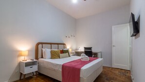 A bedroom with a bed, bedside tables, a desk, a chair, a television, and a door. - 15min From Flamengo Beach Oc107b (Rio de Janeiro)