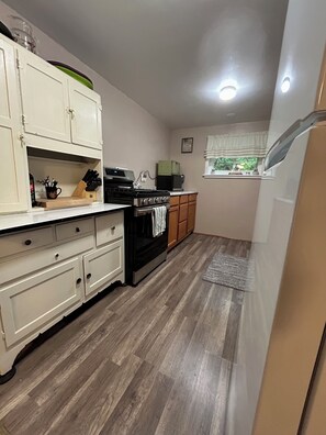 A compact kitchen with white cabinetry, a black stove, and a window with a view.
