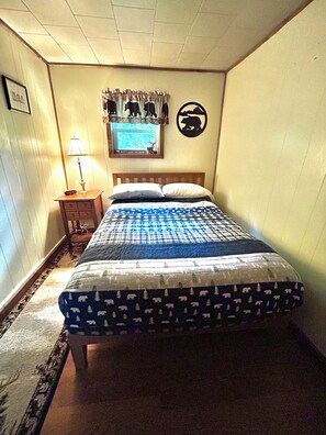 A bedroom with a bed, a nightstand with a lamp, a framed picture, and a wall decoration.