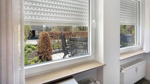 Una ventana con persianas, un radiador debajo, y vistas a muebles y plantas de exterior.
