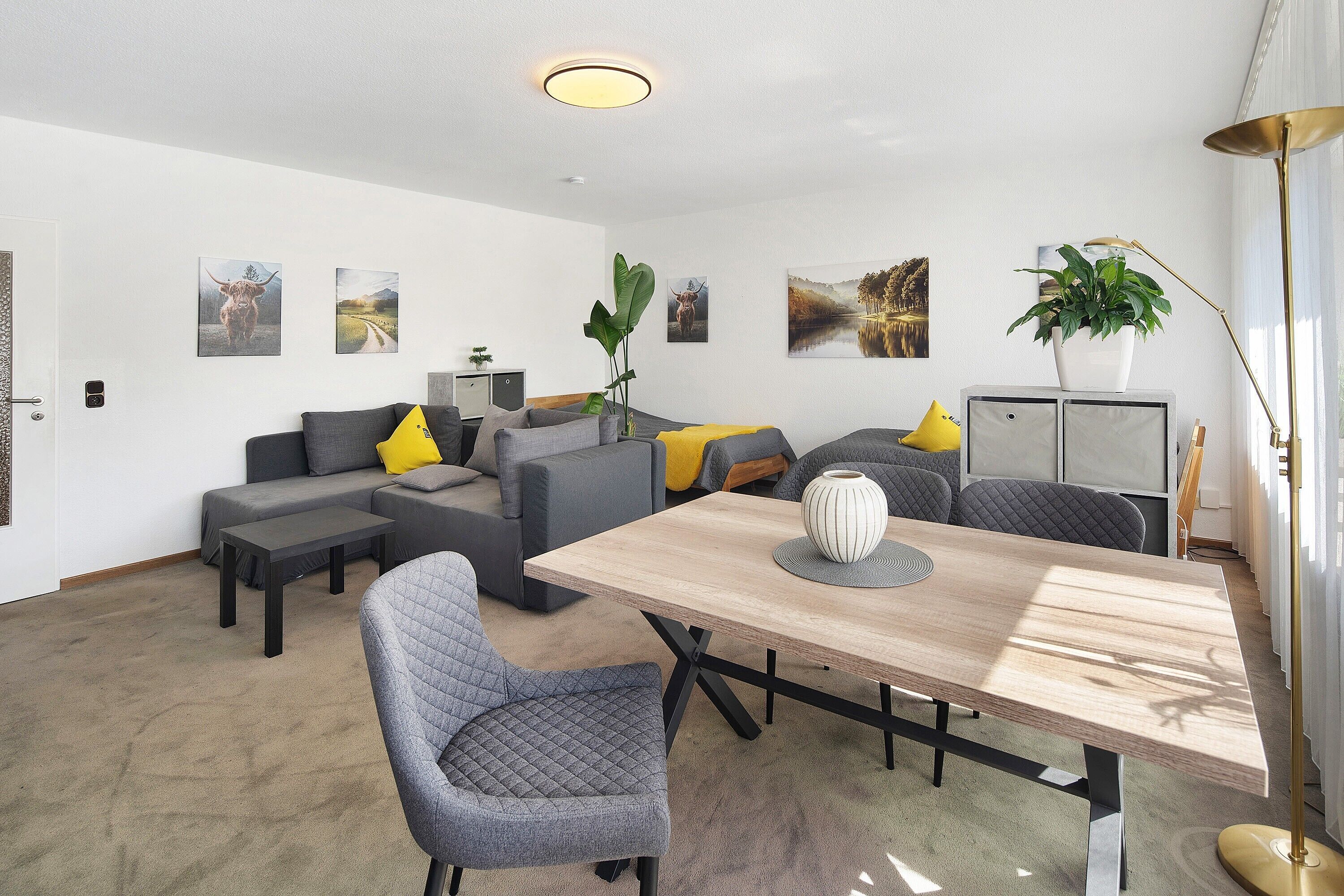 Een moderne woonkamer met een bank, een eettafel en een salontafel. Er hangen kunstwerken aan de muur en staat een kamerplant.