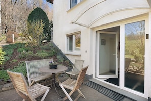 Eine Terrasse mit Tisch und Stühlen, eine Glasschiebetür und ein Garten mit Pflanzen.