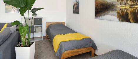 Un dormitorio con dos camas, una planta grande en maceta y un cuadro en la pared.