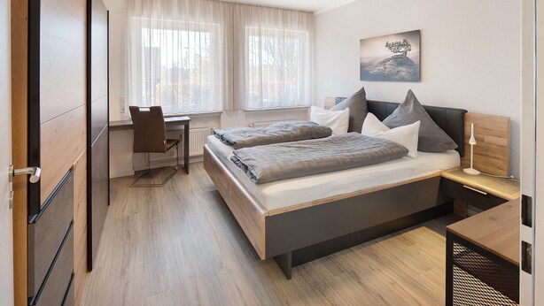 Un dormitorio con cama, mesitas de noche, un escritorio y una silla.
