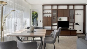 Una sala de estar moderna con una mesa de comedor, sillas tapizadas grises, un televisor de pantalla plana y un armario empotrado de madera.