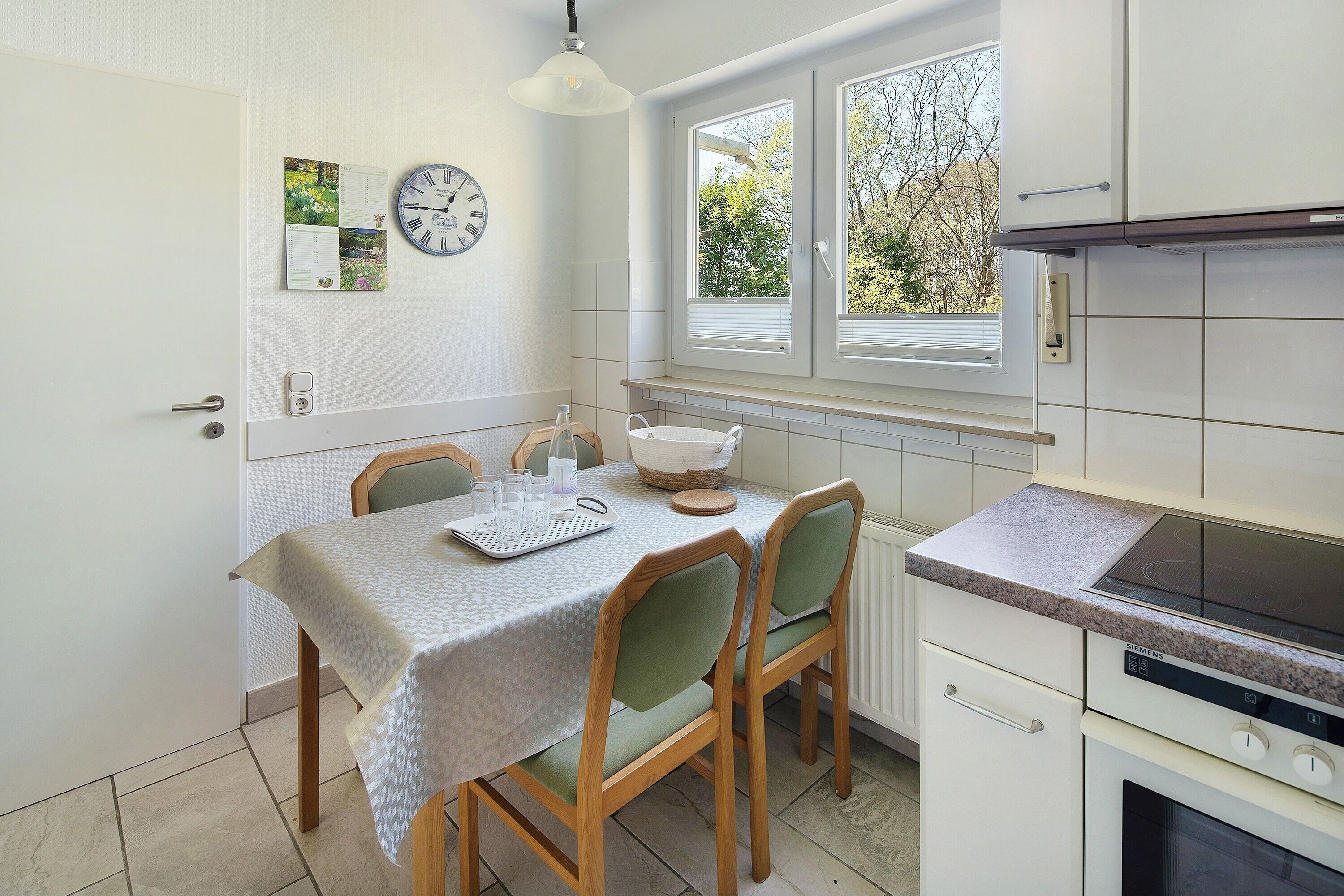 A kitchen with a dining table, chairs, a clock, and a window with blinds.