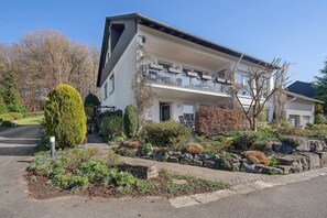 Ein zweigeschossiges Wohngebäude mit Balkon, einer Steinmauer und einem angelegten Garten.