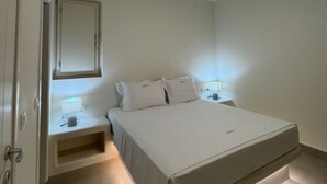 Makuuhuone, jossa on sänky, yöpöydät, peili ja kattovalaisin.