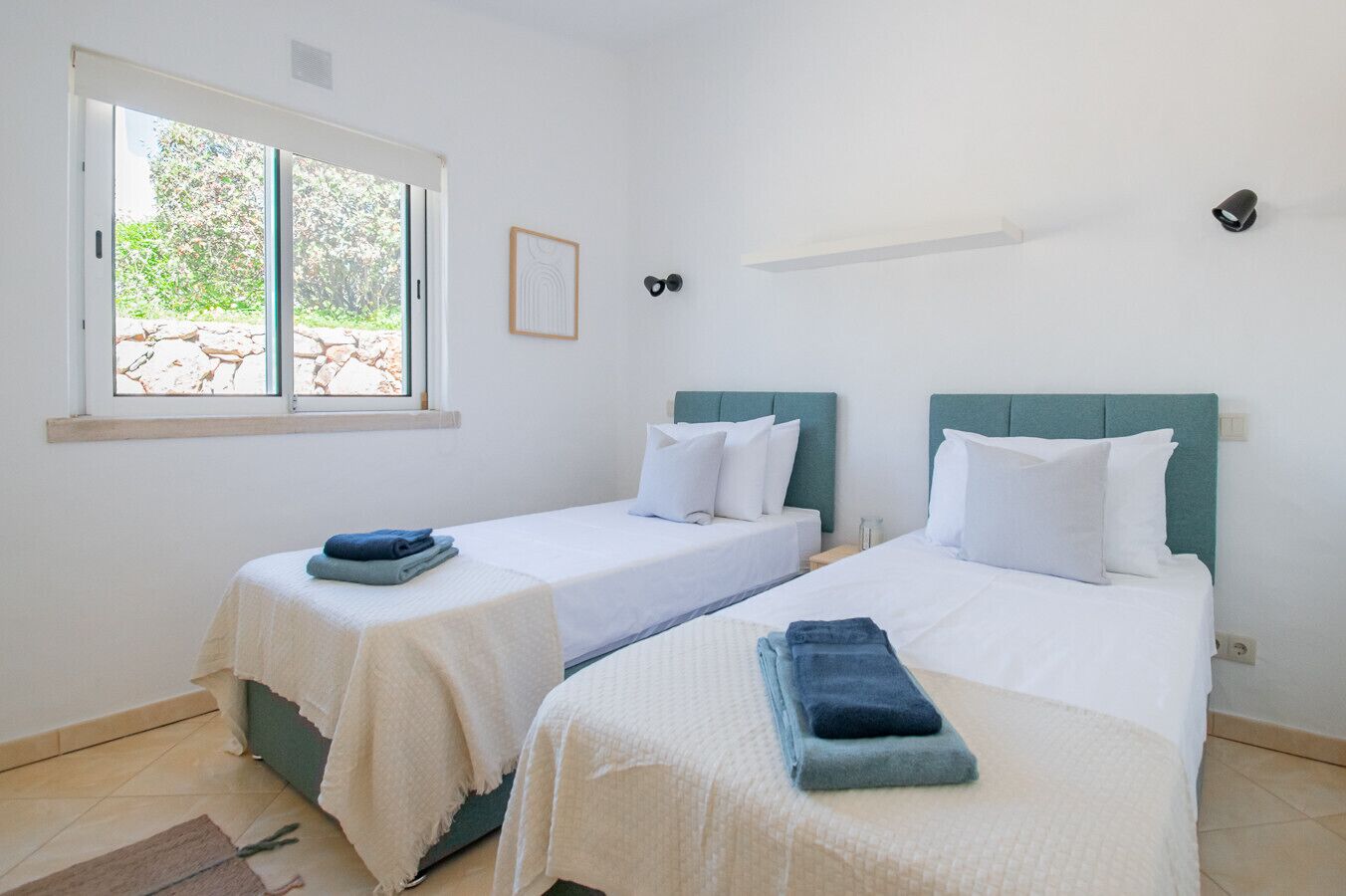Una habitación con dos camas, una ventana con vistas y un estante pequeño.