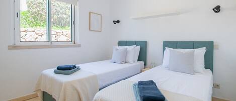 Una habitación con dos camas, una ventana con vistas y un estante pequeño.